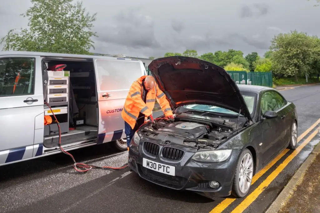 Breakdown recovery technician jump-starting a BMW with a battery charger, bonnet open on roadside in Coventry"